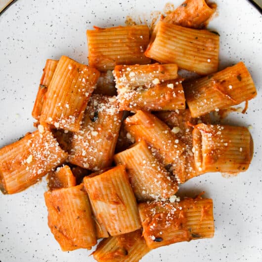 spicy sausage pasta on a white plate sprinkled with parmesan cheese