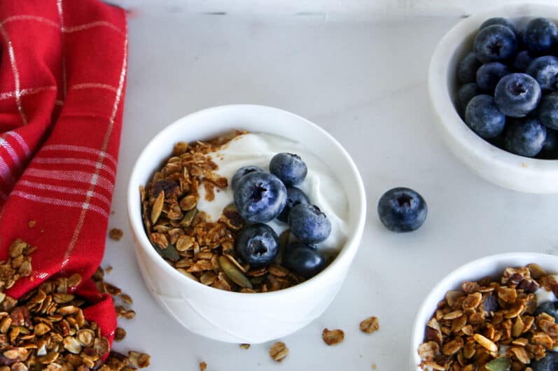 gingerbread granola in bowls with a bowl of blueberries