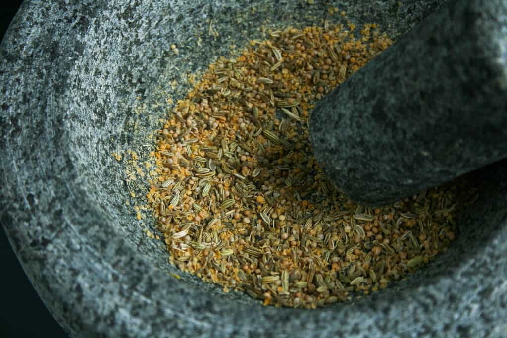 Fennel seeds and mustard seeds crushed in a mortar and pestle