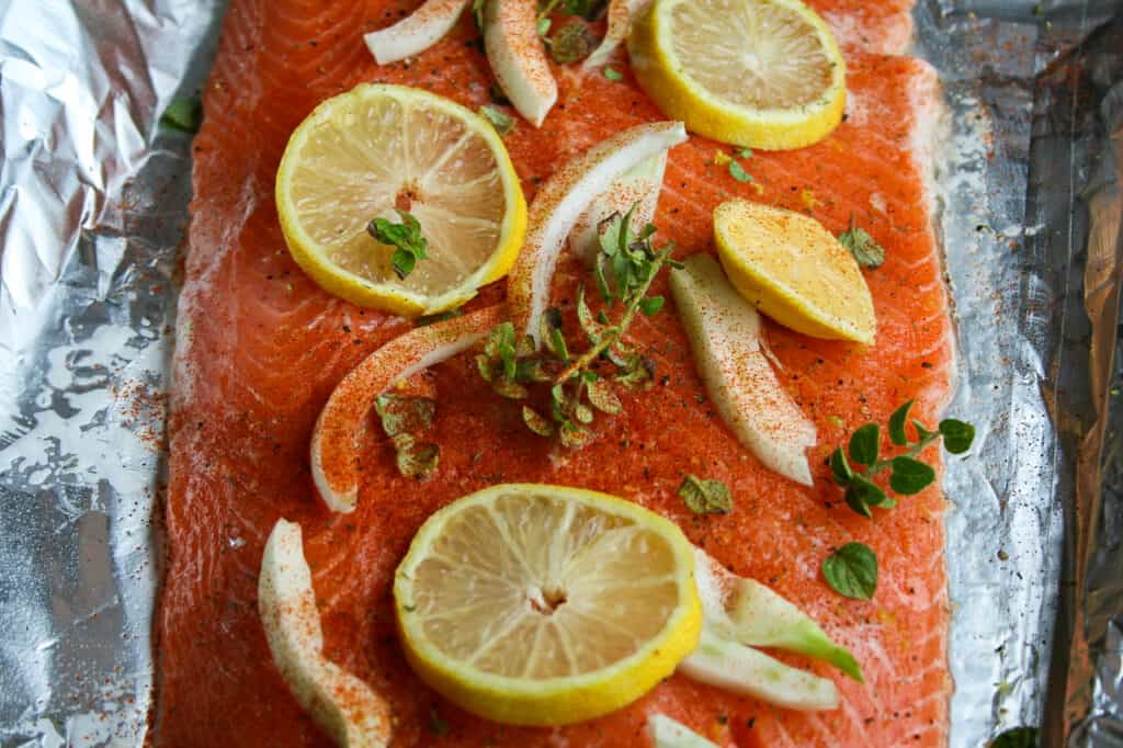 Uncooked Salmon with oregano, lemons, and fennel. Photographed on a tinfoil lined baking tray