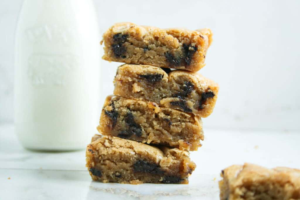 Crinkle Top Blondies with chocolate chips stacked on top of each other with a glass of milk in the background