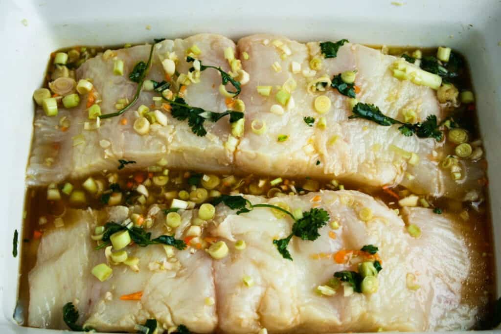 Citrus and Habanero Poached Sea Bass Marinading in a white baking dish