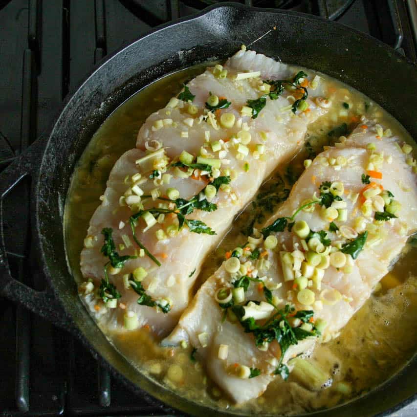 Citrus and Habanero Poached Halibut. Uncooked Halibut filets on the stove in a cast iron skillet ready to be poached