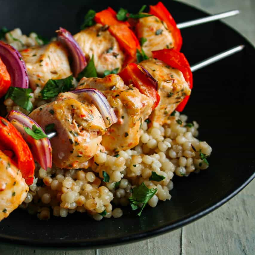 Greek Chicken Kebabs with red bell peppers and red onion served in a black bowl with couscous