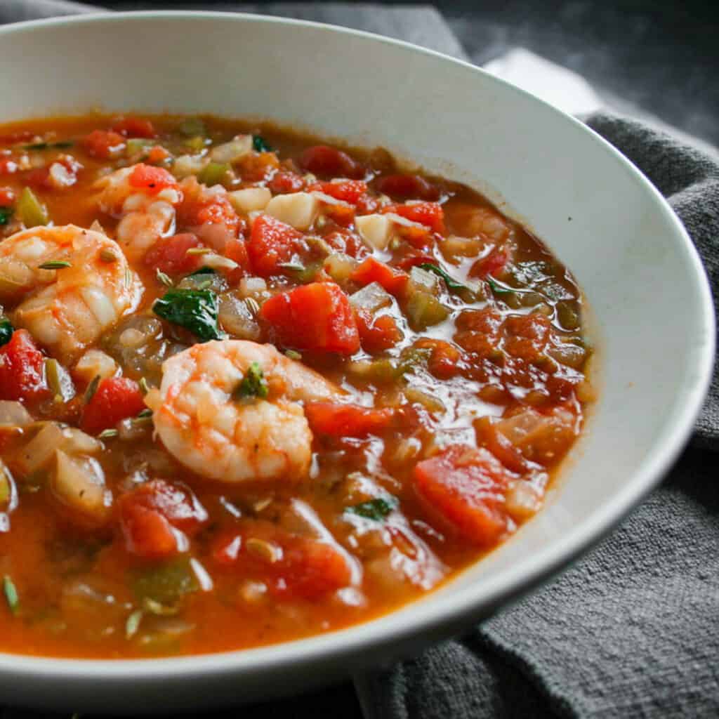 Close up photograph of seafood cioppino in a white bowl with a grey napkin