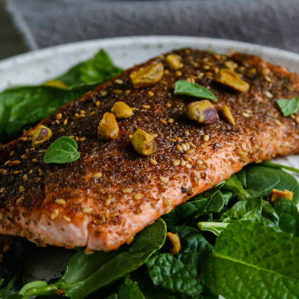 Close up photograph of za'atar crusted salmon on a plate of spinach with fresh herbs