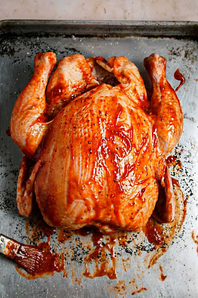 Whole Chicken with Chipotle Raspberry BBQ Sauce. on a baking tray ready to be grilled.