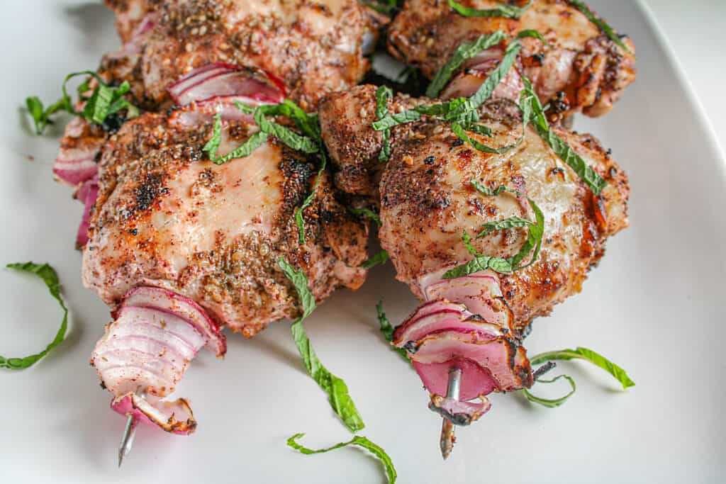 Za'atar Grilled Chicken Thighs on a white serving platter garnished with fresh mint