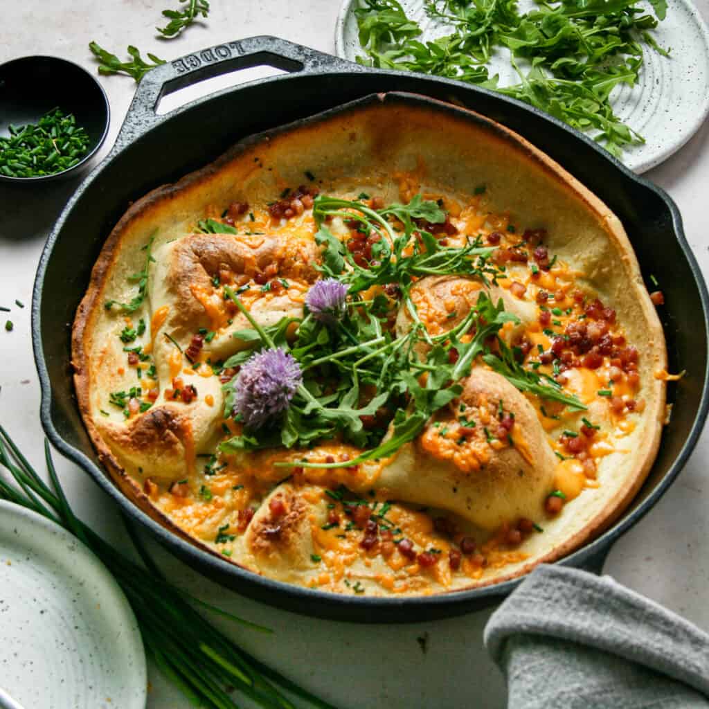 Cheddar and Chive Savory Dutch Baby in a cast iron skillet with arugula on top