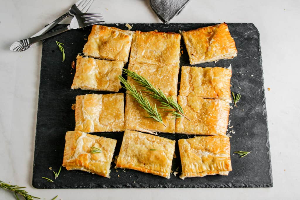 Spiced Honey Whipped Feta Pastry. Cut into squares. Photographed on a slate cheese board. Garnished with fresh rosemary sprigs