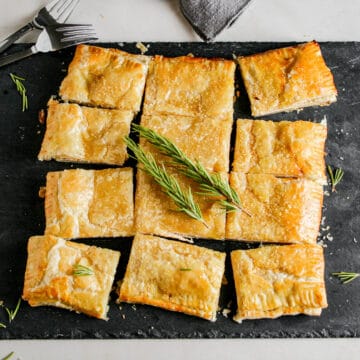 Spiced Honey Whipped Feta Pastry. Cut into squares. Photographed on a slate cheese board. Garnished with fresh rosemary sprigs