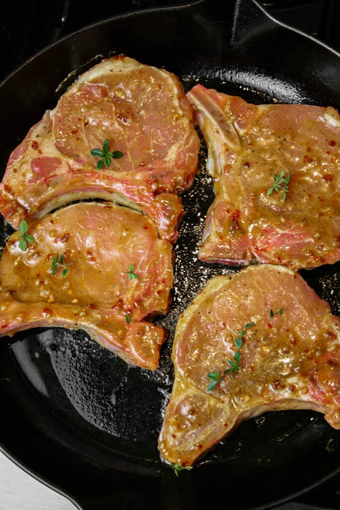 Pan Seared Maple Pork Chop photographed cooking in a cast iron Staub skillet. the skillet is black. there is a maple sauce on the pork chops