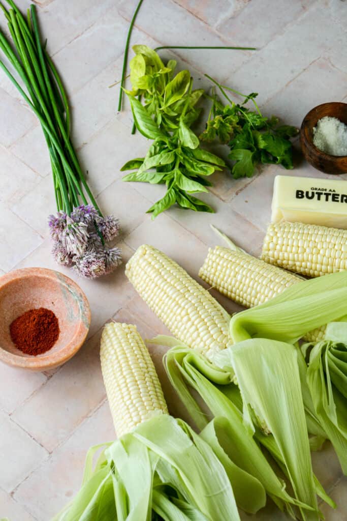 Ingredients for Grilled corn on the cob with herbed garlic butter. Photographed on tile