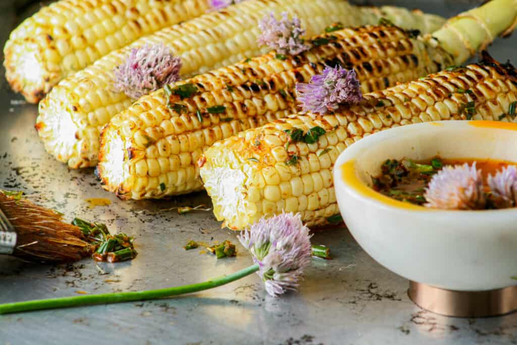 Grilled corn on the cob with herbed garlic butter. Photographed on a metal baking tray.