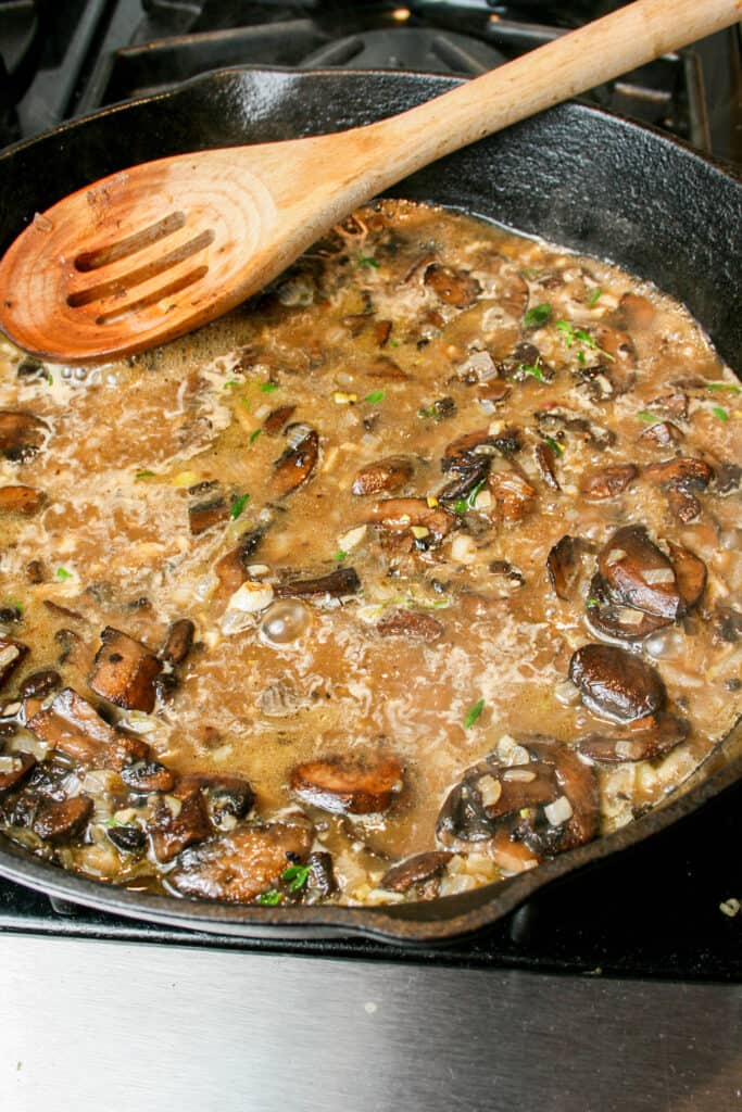 Process photograph of Creamy Mushroom Pasta with Burrata. Mushrooms, shallots, garlic, and thyme cooking in beef broth