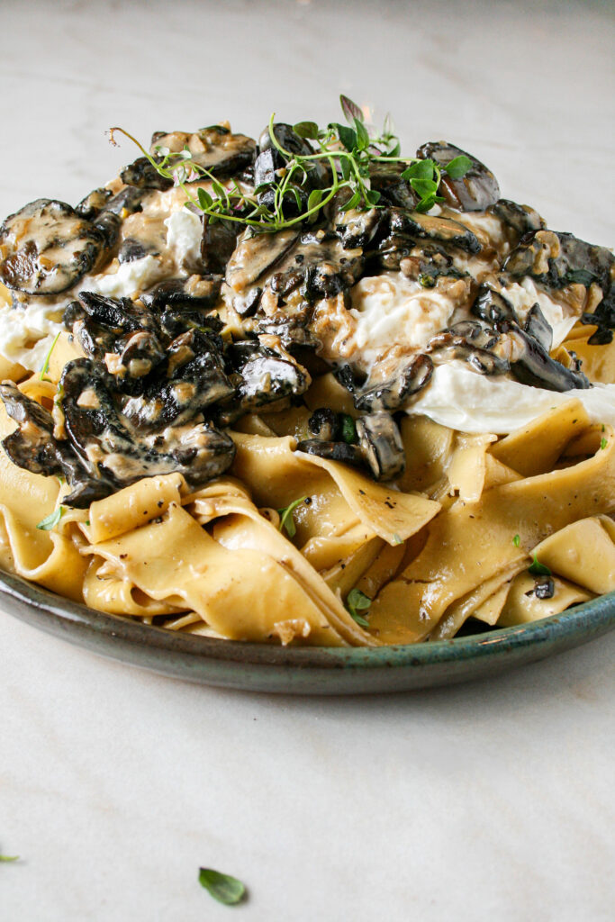 Photograph of Creamy Mushroom Pasta with Burrata. pictured on a green plate on top of marble counter top