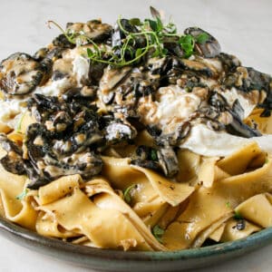 Photograph of Creamy Mushroom Pasta with Burrata. pictured on a green plate on top of marble counter top