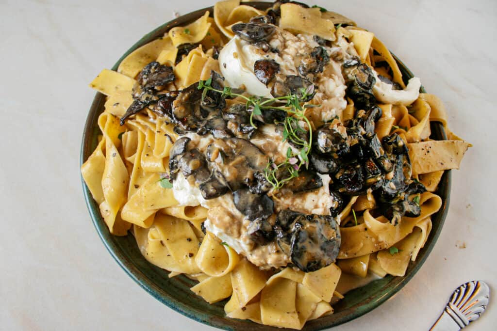 Photograph of Creamy Mushroom Pasta with Burrata. pictured on a green plate on top of marble counter top