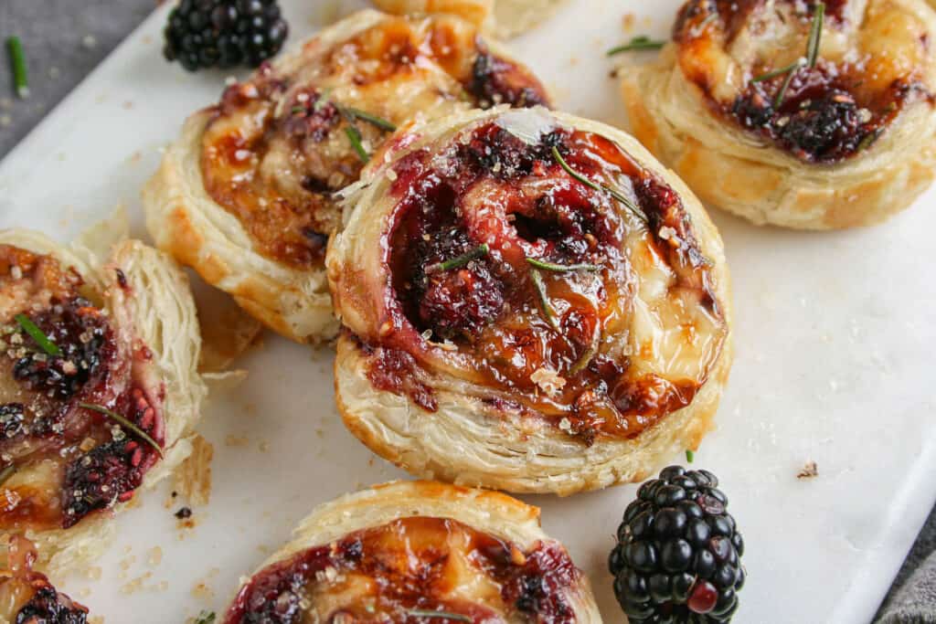 Photograph of Blackberry Brie Pinwheel on a marble serving board. with blackberries