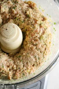 Process shot of lemongrass, ginger, cilantro, green onions blended, and ground chicken in a food processor for Thai meatballs