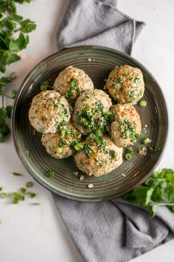 Thai meatballs served on a green pottery dish on top of a gray napkin.