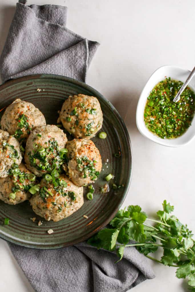 Thai meatballs photographed on a green platter on top of a gray napkin. ramekin of zesty Thai dipping sauce is to the side