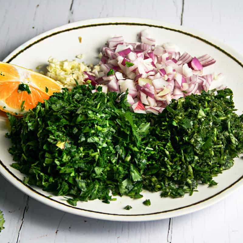 Ingredients for chimichurri. Pictured is chopped parsley, chopped shallots, minced garlic, and lemon juice