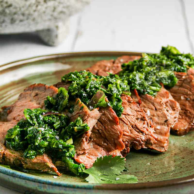 Flank Steak with Chimichurri. Photographed on a green plate on top of a white wood background