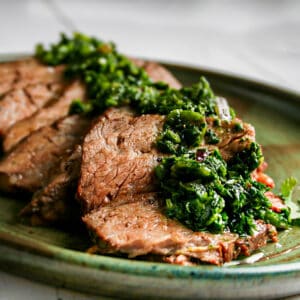 Flank Steak with Chimichurri. Photographed on a green plate on top of a white wood background