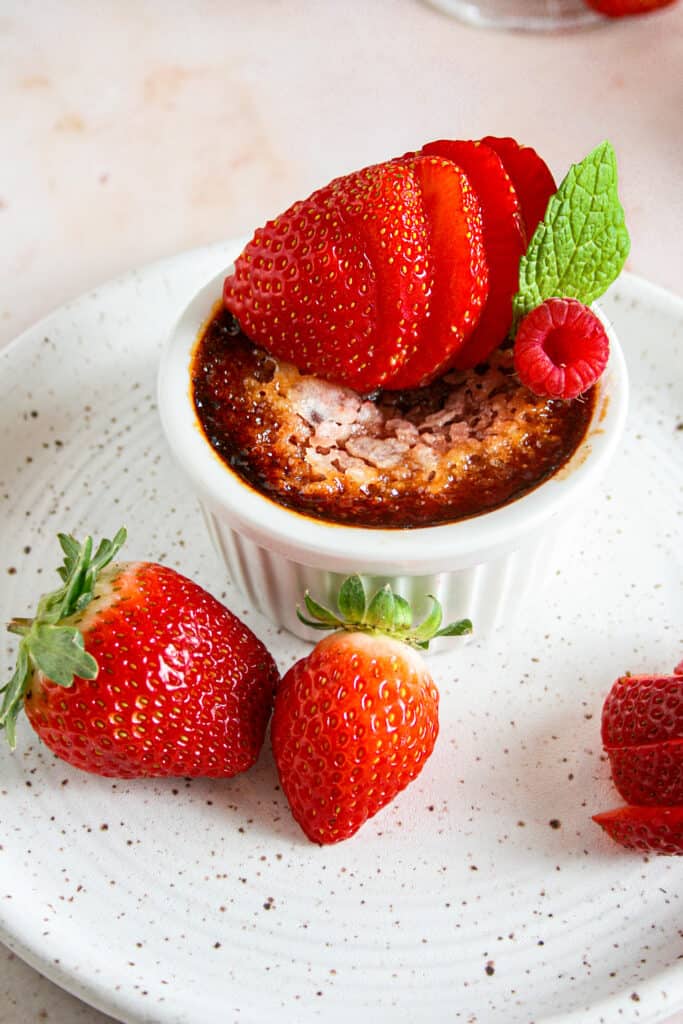 Red Velvet Creme brulee photographed on a white ceramic plate. Garnished with strawberries