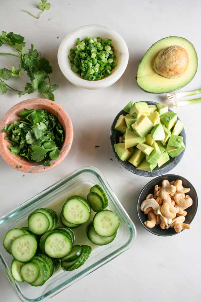 Toppings for spicy salmon rice bowl. Includes, cucumbers, cilantro, green onions, avocado, and cashews