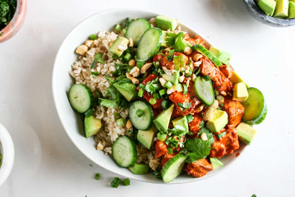 Spicy Salmon rice bowl with brown rice, salmon cubes, cucumbers, cilantro, green onions and cashews
