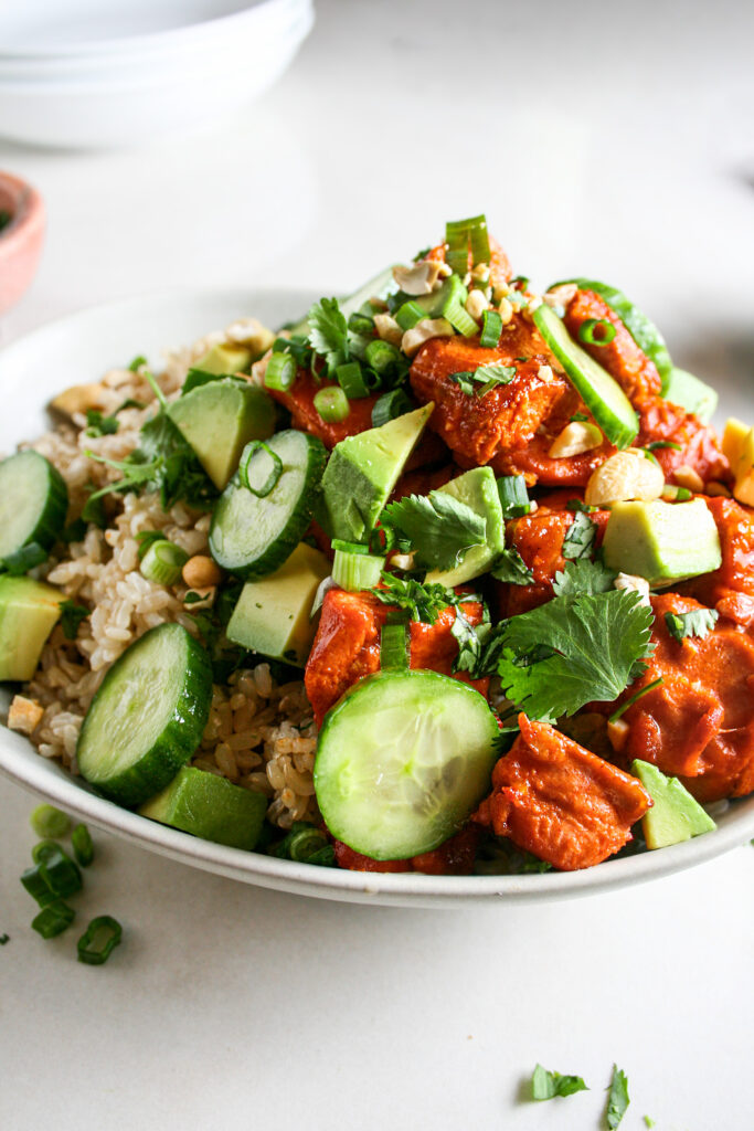 Spicy salmon rice bowl with toppings of cucumber, cilantro, cashews, green onions