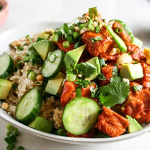 Spicy salmon rice bowl with toppings of cucumber, cilantro, cashews, green onions