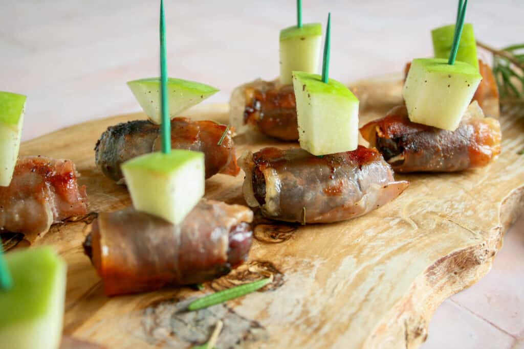 prosciutto wrapped dates with an apple slice on a wooden cutting board