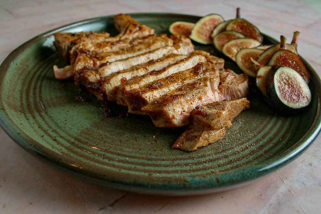 Pork Chops with spicy fig sauce sliced on a green plate with fresh figs.