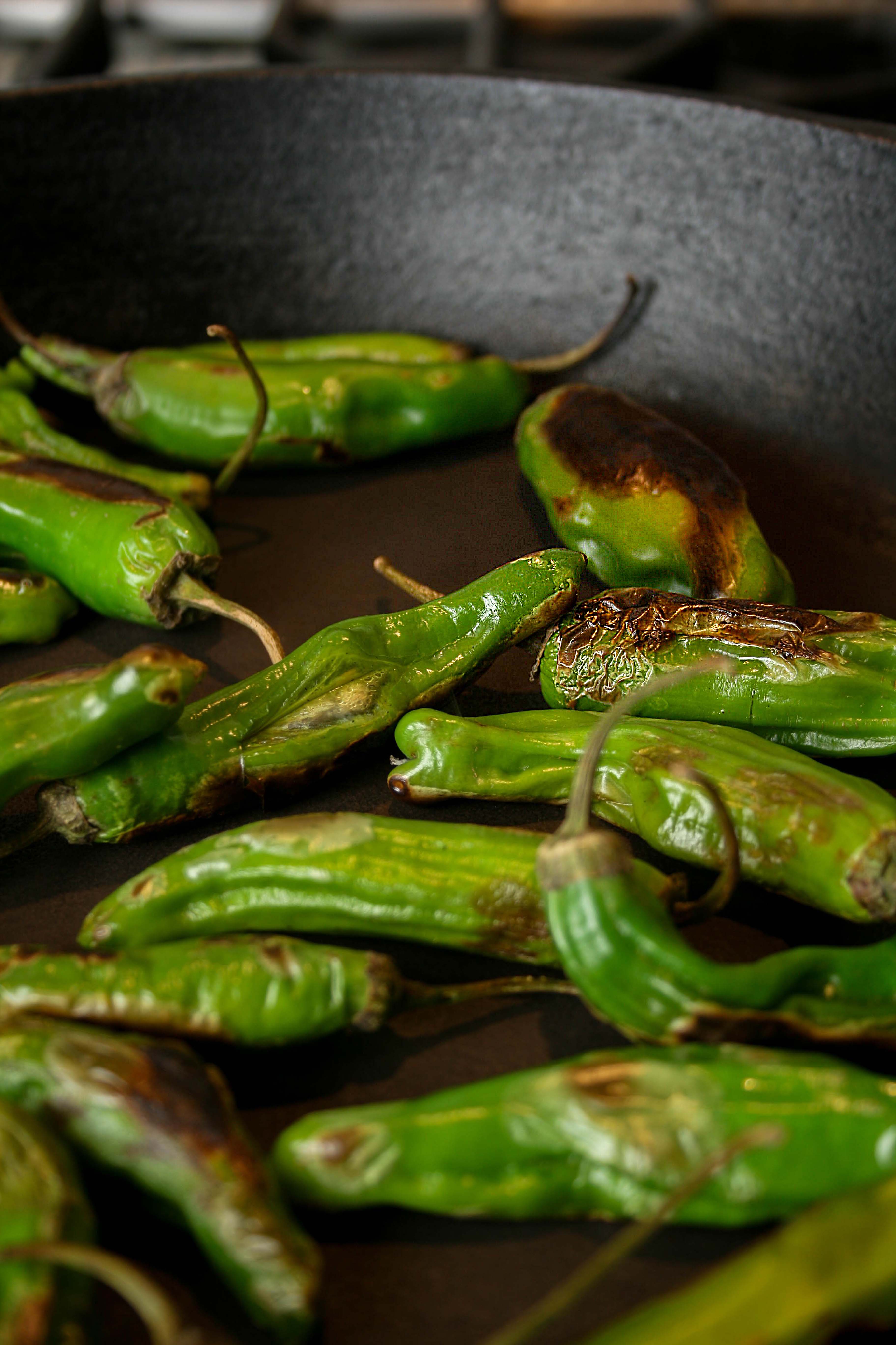 close up photograph of charred shishito pepper on a cast iron skillet